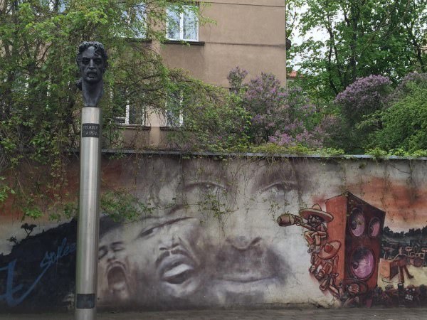 A bust of Frank Zappa sits on a plinth in front of a mural. 